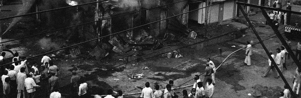 Sikh-owned shops burn as a mob looks on. Delhi, November 1984.